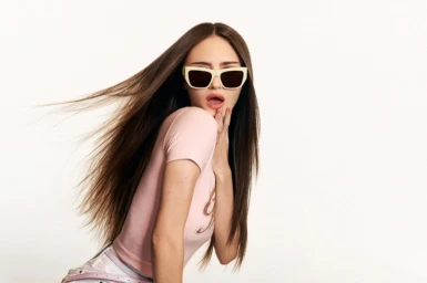 Model Leni Klum wearing white sunglasses and a pink top with hair blowing against a white background for Guess.