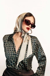 Model Leni Klum wearing a patterned silk headscarf, sunglasses, and printed blouse against a bright white backdrop