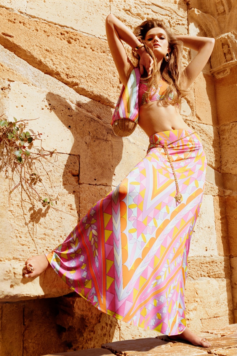 Model Lulu Tenney in a vibrant geometric printed maxi skirt and top posing against a sunlit stone wall.