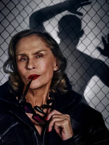 Lauren Hutton wearing sunglasses and a black leather jacket against a chain-link fence background.