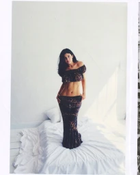 Kylie Jenner wearing a leopard print two-piece set standing on a white bed against a plain backdrop.