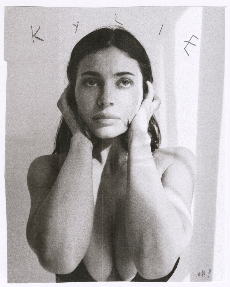 Monochrome portrait of Kylie Jenner holding her hands to her face against a plain background