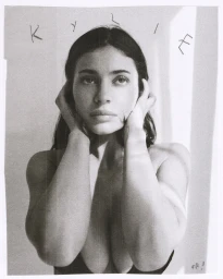 Monochrome portrait of Kylie Jenner holding her hands to her face against a plain background