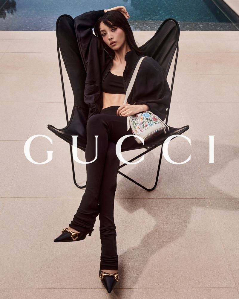 Woman in black outfit seated in a black butterfly chair beside a pool for Gucci Monte Carlo Summer 2026 campaign.