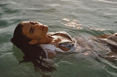 Model floating on her back in calm ocean water wearing a patterned bikini and white shirt