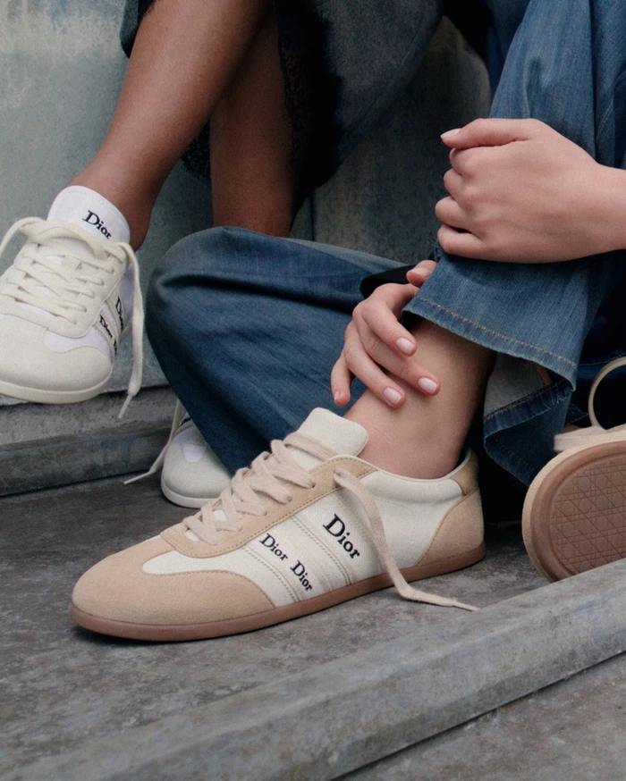 Close-up shot of cream and tan Dior sneakers with branded ribbons worn with blue jeans