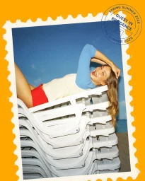 Gigi Hadid lying across a stack of white loungers against a blue sky backdrop for Guest In Residence.