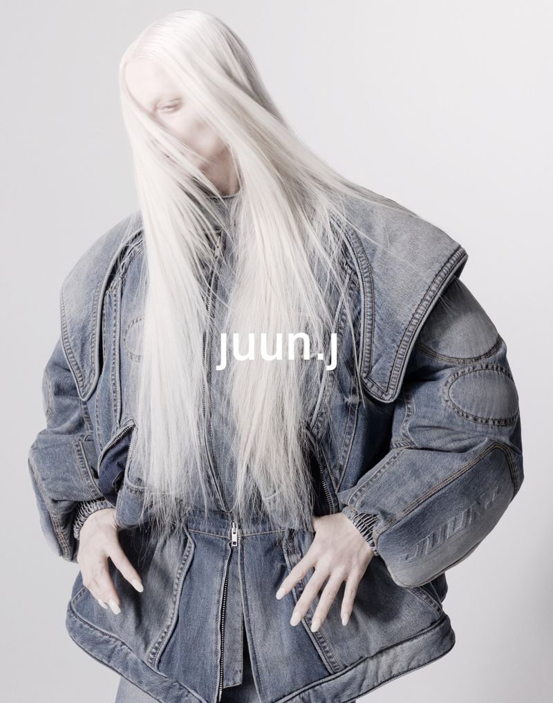 Fashion-forward photo of a model with long platinum hair wearing an oversized denim jacket against a bright studio backdrop.