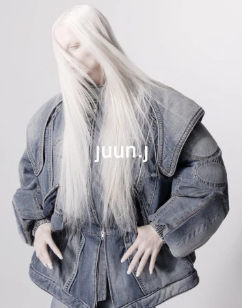 Fashion-forward photo of a model with long platinum hair wearing an oversized denim jacket against a bright studio backdrop.
