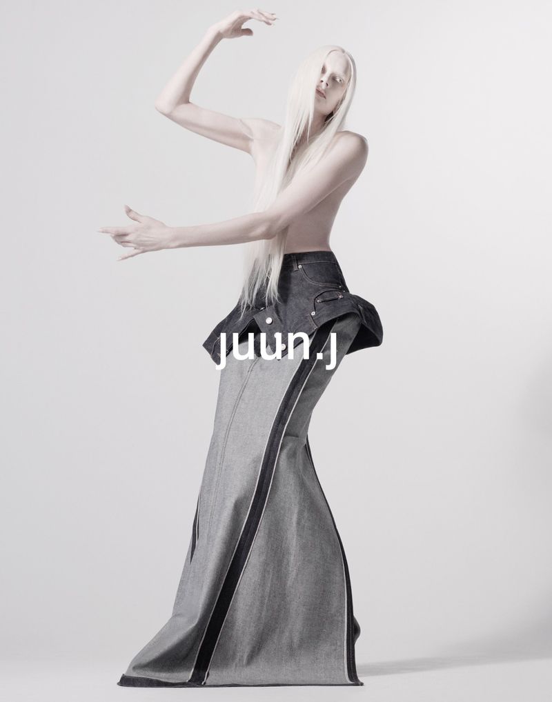 Fashion photo of androgynous model in dramatic denim skirt and bare chest against a neutral backdrop, showcasing avant-garde design and styling.