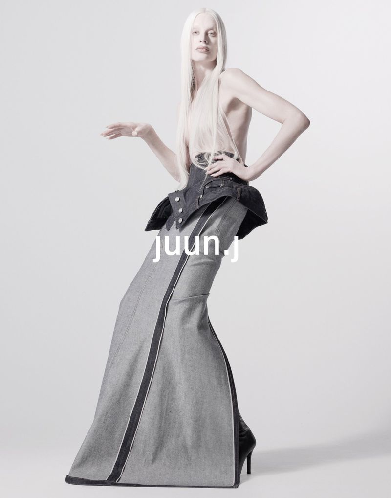 A slender fashion model with pale skin and long white hair poses in a denim-inspired couture outfit against a bright white background.