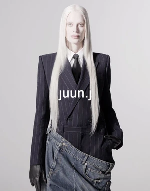 Model with long white hair wearing a pinstripe suit jacket and layered denim against a light grey studio background.