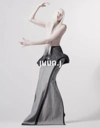 Kristen McMenamy posing topless in an architectural denim maxi skirt against a bright white studio backdrop.