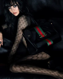 Ningning in black mesh monogram bodysuit holding a Gucci leather handbag with red and green stripe against a dark background