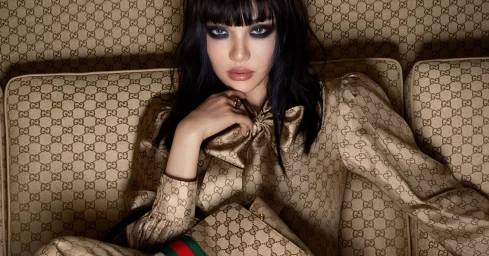 NINGNING wearing a monogram Gucci blouse and holding a Gucci handbag while seated on a matching sofa