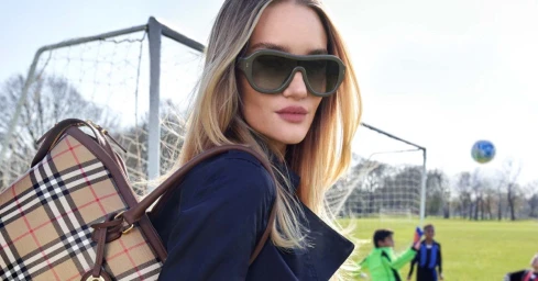 Rosie Huntington-Whiteley wearing oversized sunglasses and carrying a plaid Burberry handbag in front of a soccer goal