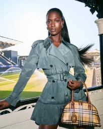 Jodie Turner-Smith wearing a teal trench coat holding a plaid handbag overlooking a sports stadium for Burberry.