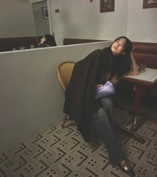 Woman seated in a cafe with tiled floor holding a lavender clutch for Dior Pre-Fall 2026 Campaign photographed by David Sims