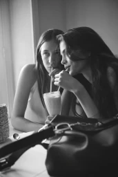 Two models drinking from a single glass with straws in a black and white campaign image for Dior.