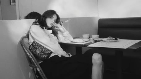 Model seated at a café table in a monochrome image wearing a patterned shoulder bag and dark skirt