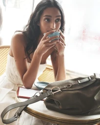 Woman in white dress drinking from a blue cup at a café table with a dark shoulder bag