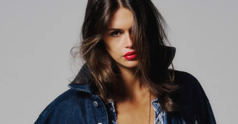 Kaia Gerber wearing a dark denim jacket against a neutral grey studio backdrop for RE