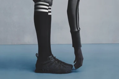Close-up of legs wearing black sneakers, striped knee-high socks, and another figure touching the shoe with a hand