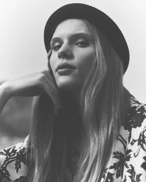Model in a dark beanie and patterned top resting chin on hand in a monochrome portrait.