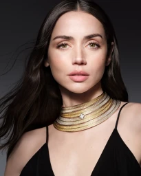 Ana de Armas wearing a layered gold and diamond choker necklace and black top against a dark background