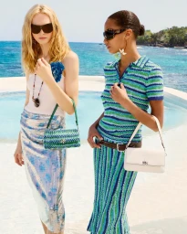 Two female models in sunglasses wearing stylish apparel stand outdoors by a swimming pool overlooking the ocean for Tory Burch Splash