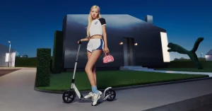 ROSÉ posing with a kick scooter wearing a Puma crop top and shorts in front of a modern dark house at dusk