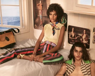 Models in striped clothing posing on a bed inside a room with ocean views out the window for Versace.