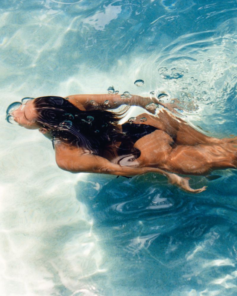 Underwater shot of a woman swimming in a pool, showcasing the clear turquoise water, body motion, and play of light through the surface.