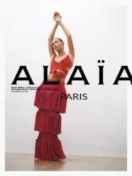 Hailey Bieber wearing a red wrap top and tiered skirt with arms raised against a plain white background for Alaïa