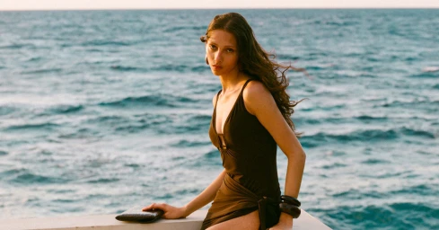 Model Yasmin Wijnaldum wearing a dark swimsuit by the ocean for Stuart Weitzman Exotic Escape campaign