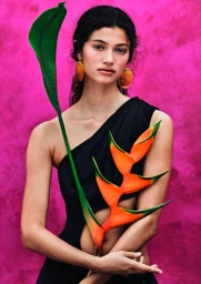Model in black top holding a bird of paradise flower against a textured pink background