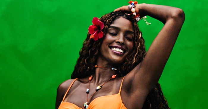 Smiling woman in an orange top with a red flower in her hair against a green background