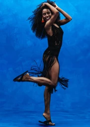 Ice Spice in black fringed dress jumping playfully against vibrant blue backdrop for H&M campaign