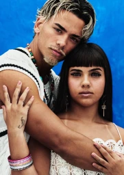 Portrait of a man with dyed blonde-tipped hair embracing a woman with dark hair and bangs against a bright blue background for H&M