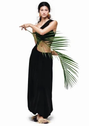 Model in black dress holding a palm frond standing against a white seamless background for H&M