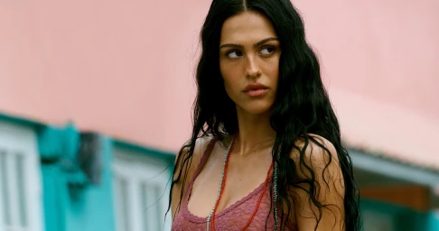 Amelia Gray wearing lace lingerie and beaded necklaces against a pink and teal building exterior.