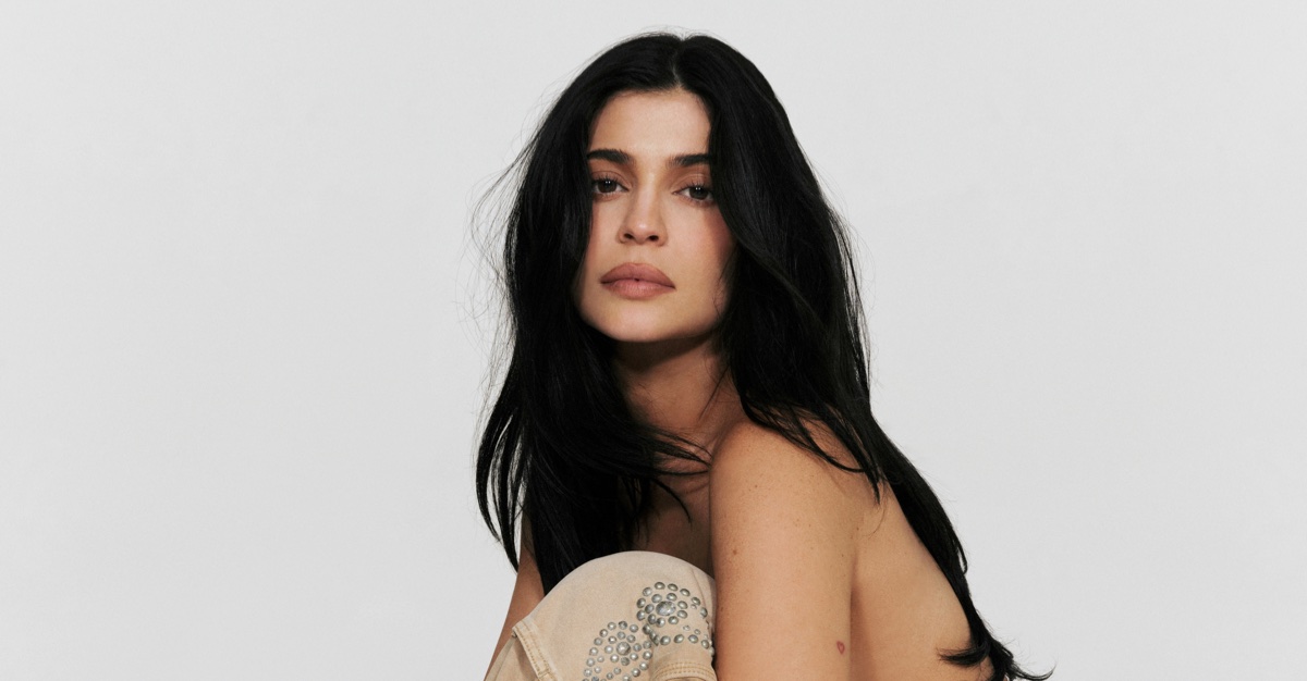 Kylie Jenner looking directly at the camera with bare shoulders and studded tan pants against a white background.