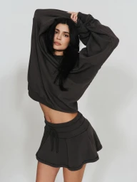Kylie Jenner wearing a dark grey sweatshirt and matching mini skirt with her arms raised against a plain white background.