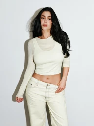 Kylie Jenner wearing cream long sleeve top and light jeans against white seamless background for Khy