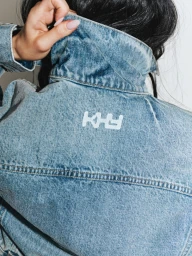 Close-up of a person wearing a light blue denim jacket with a white KHY logo printed on the back collar