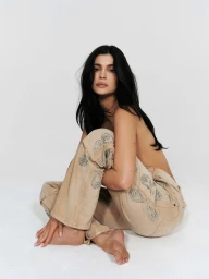 Kylie Jenner sitting on a white studio floor wearing embellished tan denim jeans for Khy Born in LA