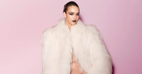 Model wearing a voluminous white faux fur coat and statement earrings against a pink background for Gucci Generation Gucci.