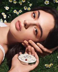 Close-up beauty portrait of Deva Cassel holding a daisy-decorated compact amid grass for Dior