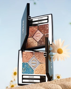 Two open Dior eyeshadow palettes featuring embossed floral patterns against a clear sky background with white daisies.