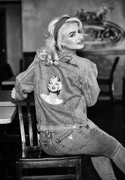 Blonde woman wearing denim jacket with Marilyn Monroe graphic seated backwards on wooden chair
